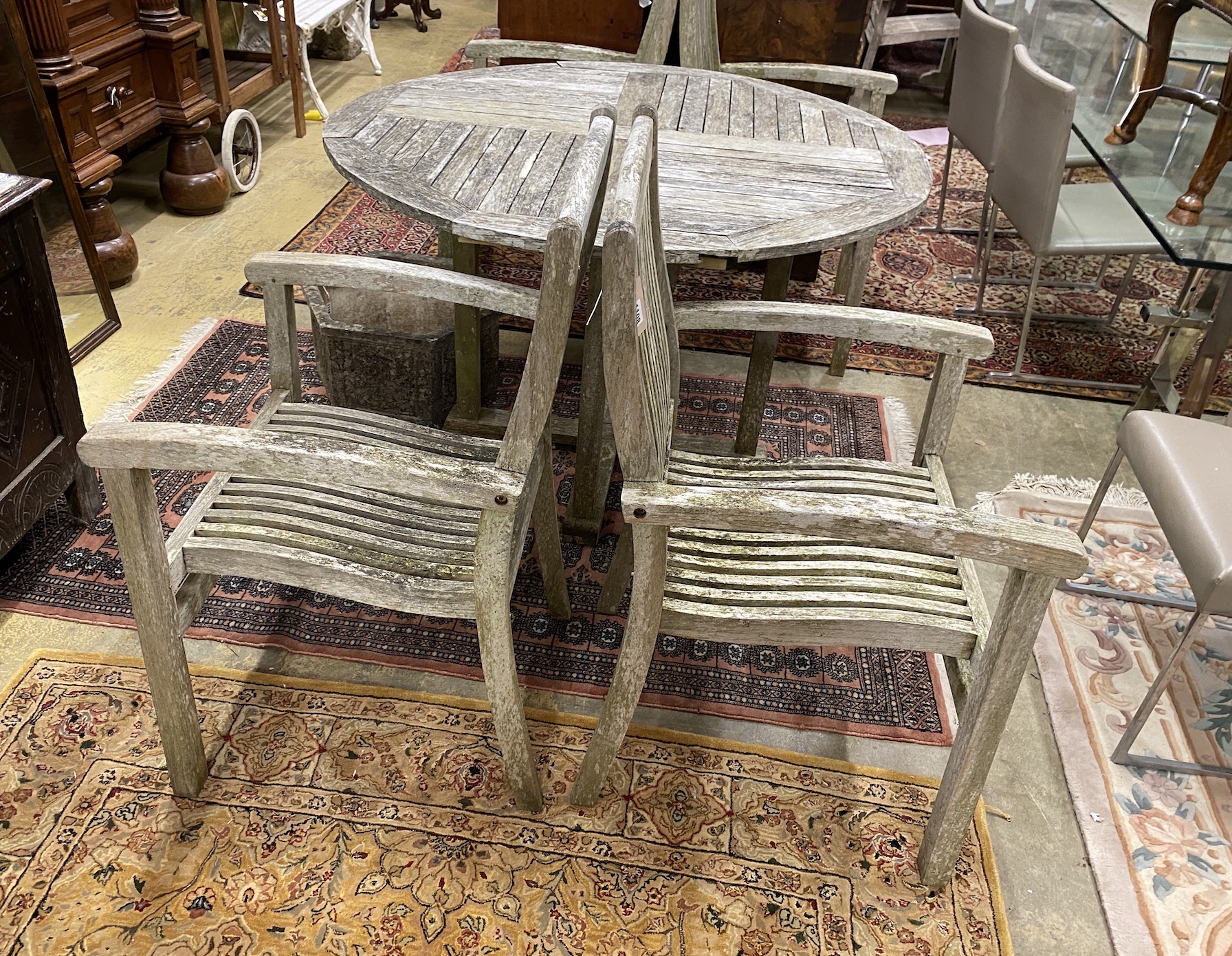 A circular weathered teak garden table, diameter 120cm, height 75cm and four elbow chairs
